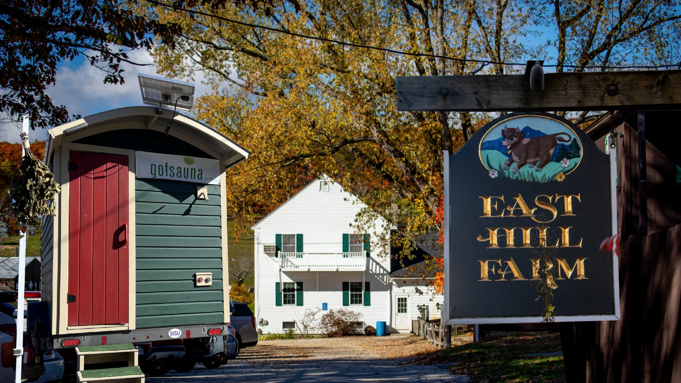 Got Sauna’s mobile sauna beside the East Hill Farm sign and autumn trees in Troy, New Hampshire